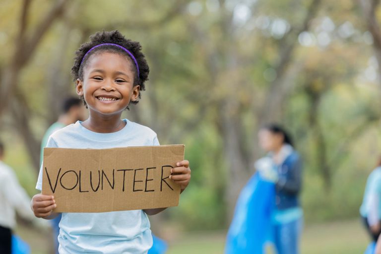 Adorable little girl holds up "Volunteer" cardboard sign outdoors